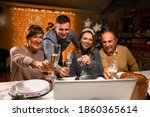 Happy family greeting their family and friends with a champagne glass, on New Year's eve using a skype video call. Relatives looking to a laptop. Social distancing during the coronavirus pandemic.