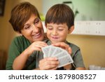 Adorable smiling couple of boy and his grandmother sitting together and smiling while they are playing a cards game. Spending quality leisure time with children and family concept.
