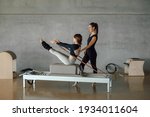Small photo of Slim fit Woman doing core exercises while taking Personal Pilates lesson on a Reformer machine, by a female instructor at a big gymnasium center, wide industrial studio. Healthy fitness lifestyle.