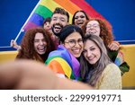 Selfie of a LGBT group of young people celebrating gay pride day holding rainbow flag together. Homosexual community smiling and taking cheerful self portrait. Lesbian couple and friends generation z