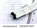 Small photo of vintage slide rule being used for calculation with technical formula on a piece of paper