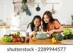 Small photo of Portrait of enjoy happy love asian family mother with little asian girl daughter child help cooking food healthy eat with vegetable testing smell soup in a pot with spoon.helping mommy in kitchen