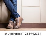 Young fashion man's legs in blue jeans and brown boots on wooden floor
