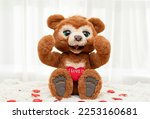 Valentine's day concept. A cute brown teddy bear with big eyes sits on a rug against a window with a bright red heart. Close-up.