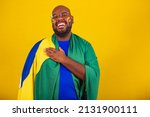 Small photo of handsome afro brazilian man wearing glasses, brazilian fan, brazil, world cup 2022, hand to chest, singing anthem is born. Brazilian music. beloved homeland. patriot.
