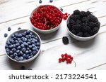 Fresh assorted berries in three plates - blueberries, blackberries and red currants on a white wooden background. Fruit, berry background.