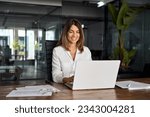 40s mid age European business woman CEO using laptop application for work sitting at table workspace in office. Smiling Latin Hispanic mature adult professional businesswoman using pc digital computer
