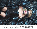 Hot dominant beautiful blonde mistress woman in shiny latex fetish corset and mask posing on bdsm accessories and fetish clothing
