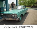 An Old Fashioned American Green colored car resembling Chevrolet Impala parked near a petrol Bunk against a green background.