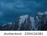 Atmospheric nightly landscape with huge snowy mountain top in dramatic sky. Hanging glacier and cornice on beautiful giant snow mountains in night. High snow-covered mountain range in dusk dim light.