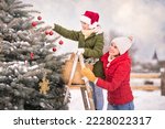 mother and daughter decorate a Christmas tree snowy winter outside