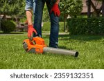Small photo of Modern leaf blower, powerful equipment for cleaning up leaf litters lying on lawn. Crop view of strong male hand in glove reaching vacuum cleaner on turf in the autumn park. Concept of seasonal work.