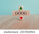 GOOG price symbol. A brick block with arrow symbolizing that GOOG index price are going down or up. Beautiful wooden table blue background. Business and gold price concept. Copy space.