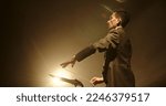 Small photo of Asian male orchestra conductor wearing tux is directing symphony orchestra with movement of his hands and stick, studio shot on black background