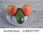 Small photo of Tomatoes and zucchini on a plate on a rustic outdoor wooden table, their arrangement resembles a phallic symbol