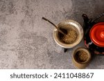 Small photo of Yerba mate tea with a small wooden mate next to a gourd filled with yerba mate, and a black teapot, on a light gray background.