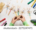 Top view of three handmade colorful funny bunnies made from wooden spoons in child hands. Small gift or decor for Easter. Easy fun kids crafts concept. 