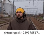 Small photo of An inattentive man walks along the rails wearing headphones. Railway danger concept