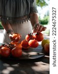 Small photo of A woman picks a bunch of tomatoes from a wooden table in the ope