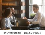 Insurance broker or salesman making offer to young millennial couple using laptop in cafe, realtor consulting customers about mortgage sitting at coffeehouse table pointing on computer screen