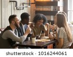 Multiracial happy young people eating pizza in pizzeria, black and white cheerful mates laughing enjoying meal having fun sitting together at restaurant table, diverse friends share lunch at meeting