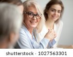 Smiling aged businesswoman in glasses looking at colleague at team meeting, happy attentive female team leader listening to new project idea, coach mentor teacher excited by interesting discussion