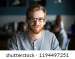 Portrait of smiling red haired millennial man looking at camera sitting in café or coffeeshop, happy young male in glasses posing for picture working at laptop or studying out in coffeehouse