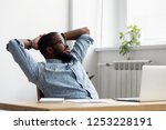 Black african millennial businessman take break during workday relaxing sitting on chair at office desk hold hands behind head looking at window thinking feels good. Stress relief daydreaming concept