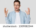Funny shocked young man nerd looking at hands showing something huge, amazed confused guy in glasses bragging with large big size exaggerating gesture isolated on white grey blank studio background