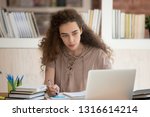 Small photo of Teen college graduate student studying looking at laptop making notes, school girl preparing for test exam writing essay project coursework doing research homework assignment learning in library