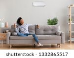 African american relaxed woman sitting on comfortable couch in living room at modern home holds air conditioner remote control enjoying breathing fresh cool air at summer or warm air at winter season