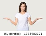 Young funny woman wearing white t-shirt stretched hands feels confused pose isolated on grey wall, girl imagining alternatives, weighs pros and cons, choosing make not easy difficult decision concept