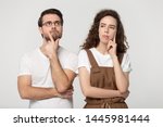 Small photo of Thinking millennial couple pose isolated on grey studio background, pretty girl handsome guy wearing glasses touch chin posture of indecision doubting feelings anxiety, deliberating brain work concept
