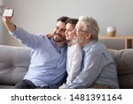 Small photo of Three generations relatives people men sitting on couch in living room, grandad grown up son grandkid using smart phone take selfie photo smiling feels happy capture the moment and parentage concept