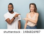 Small photo of Stressed multicultural young man and woman isolated on blue studio background point finger at each other, surprised frustrated african American male and Caucasian female blame accuse one another