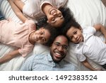 Small photo of Cheerful carefree african full family lying down on bed smiling looking at camera feels happy spending time together close up top view portrait, responsibility, parentage, devotion endearment concept