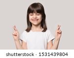 Small photo of Smiling superstitious little girl isolated on grey studio background cross fingers close eyes make wish, happy cute small child believer make gesture hope believe ask for good luck, faith concept