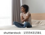 Upset sad African American woman sitting in bed alone, hugging herself, feeling lonely, unhappy girl has psychological troubles, trauma, thinking about problem in bedroom, unwanted pregnancy