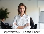 Headshot portrait of confident young businesswoman stand forefront with arms crossed looking at camera, successful millennial female ceo or boss posing for picture in office, leadership concept