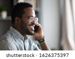 Smiling young adult african american hipster business man professional making business call talking on the phone in office enjoying corporate mobile conversation indoors, closeup side profile view