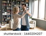 Small photo of Happy senior woman dancing with grown-up son enjoy family weekend at home together, smiling middle-aged 70s mother waltz sway with adult man child, relax in living room, family bonding concept