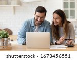 Small photo of Happy young couple planning budget, reading good news in email, refund or mortgage approval, smiling woman and man looking at laptop screen, checking finances, sitting at table at home together