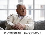 Small photo of Pensive old man resting at home sitting on couch in living room alone. Aged 80s baby boomer older generation male lost in sad thoughts feels lonely, recollect life moments has nostalgic mood concept
