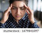 Close up exhausted Indian girl touching forehead, unhappy upset girl suffering from strong headache or migraine, overworked tired young female feeling pain in head, health problem concept