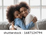 Seated on sofa african loving mother strong cuddles little daughter gives her love and caress show sincere candid feelings, concept of adopted kid and new caring mom, dear special person and affection