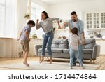 Full length overjoyed family of four jumping to music in modern studio living room. Excited young married couple dancing with playful little children siblings, spending active free time at home.