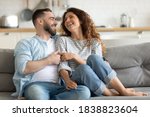 Happy married young couple hugging, sitting on cozy couch together, overjoyed laughing woman and man having fun, enjoying leisure time, relaxing on sofa in living room at home, good relationship