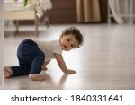 Portrait of cute little african American baby toddler crawl make first steps on home wooden floor. Small biracial newborn infant child learn walking play indoors. Childcare, upbringing concept.