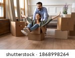 Overjoyed couple renters have fun ride in cardboard box relocate at new home together. Happy man and woman tenants engaged in funny activity feel playful on moving day. Relocation, rental concept.