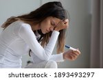 Close up unhappy upset woman holding pregnancy test, touching forehead, feeling depressed and hopeless, confused frustrated young female shocked by result, bad news, health problem concept